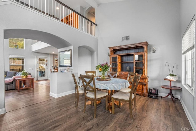 dining space with a towering ceiling and dark wood-type flooring