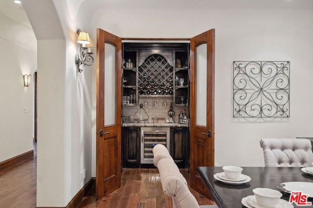 bar featuring dark hardwood / wood-style flooring, backsplash, light stone countertops, and beverage cooler