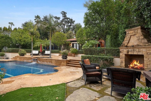 view of swimming pool featuring an outdoor stone fireplace and a patio area