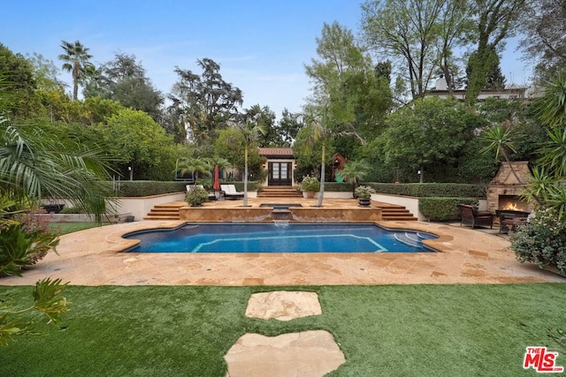 view of swimming pool featuring an outbuilding, a patio area, and an outdoor stone fireplace