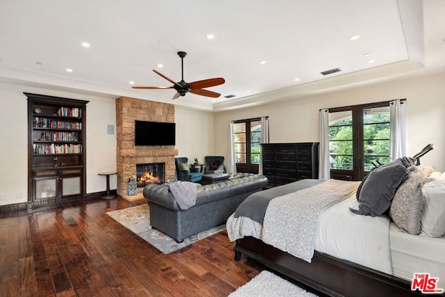 bedroom with a tray ceiling, a fireplace, dark hardwood / wood-style floors, and ceiling fan