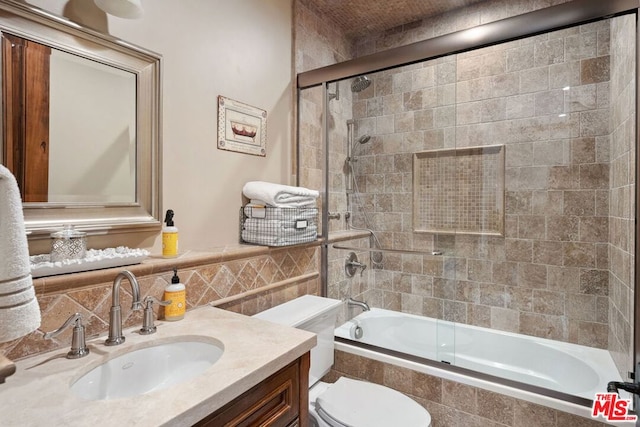 full bathroom with vanity, toilet, combined bath / shower with glass door, and tile walls