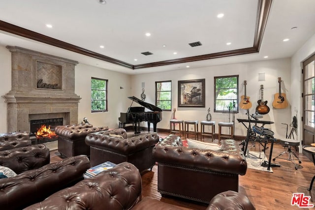 living room featuring a raised ceiling, wood-type flooring, crown molding, and a high end fireplace