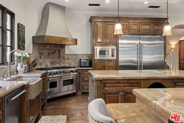 kitchen featuring premium range hood, sink, built in appliances, and light stone counters