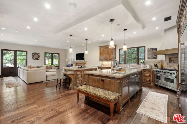 kitchen featuring premium range hood, dark hardwood / wood-style floors, an island with sink, hanging light fixtures, and stainless steel appliances