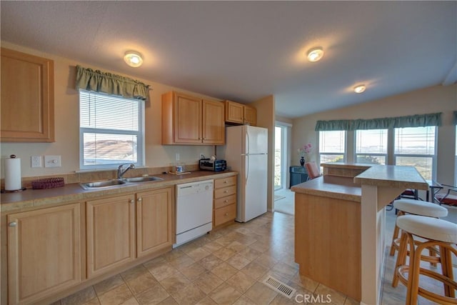 kitchen with white appliances, a kitchen breakfast bar, light brown cabinetry, and sink