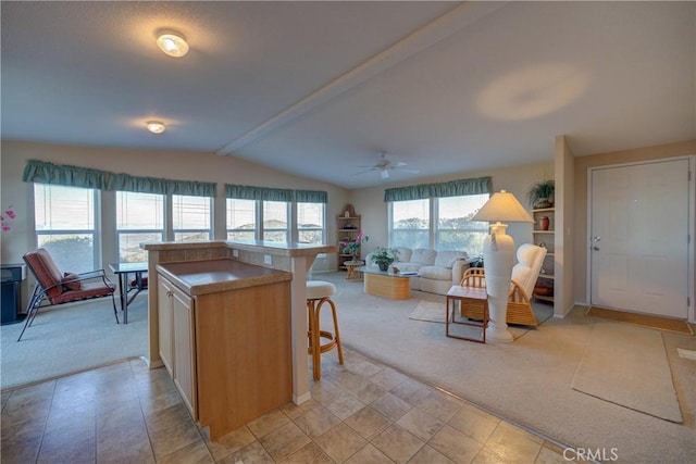 kitchen with a kitchen island, light brown cabinetry, lofted ceiling with beams, a kitchen breakfast bar, and light colored carpet