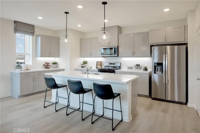 kitchen featuring sink, hanging light fixtures, light hardwood / wood-style flooring, an island with sink, and stainless steel appliances