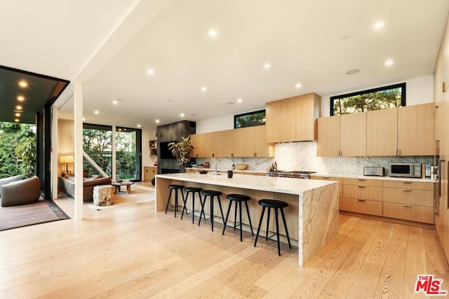 kitchen with a breakfast bar, light wood-type flooring, light brown cabinets, a large island with sink, and backsplash