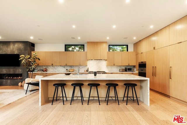 kitchen featuring a large island with sink, tasteful backsplash, a breakfast bar, and light wood-type flooring