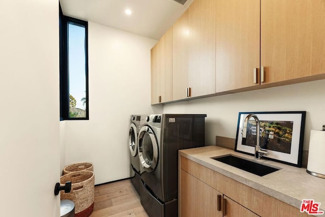 laundry area featuring cabinets, light hardwood / wood-style floors, sink, and washing machine and clothes dryer