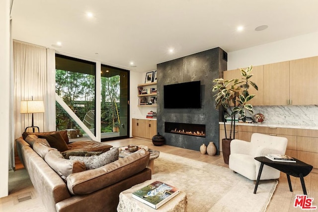 living room with a wall of windows, a large fireplace, and light hardwood / wood-style flooring