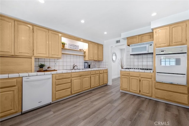 kitchen featuring sink, white appliances, light hardwood / wood-style flooring, backsplash, and tile counters