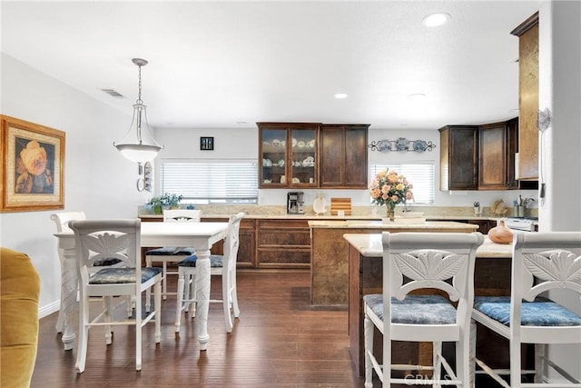 kitchen featuring dark wood-type flooring, a kitchen bar, dark brown cabinets, a kitchen island, and decorative light fixtures