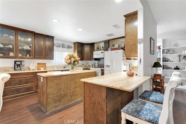 kitchen with dark brown cabinetry, a breakfast bar area, a center island, dark hardwood / wood-style floors, and white appliances