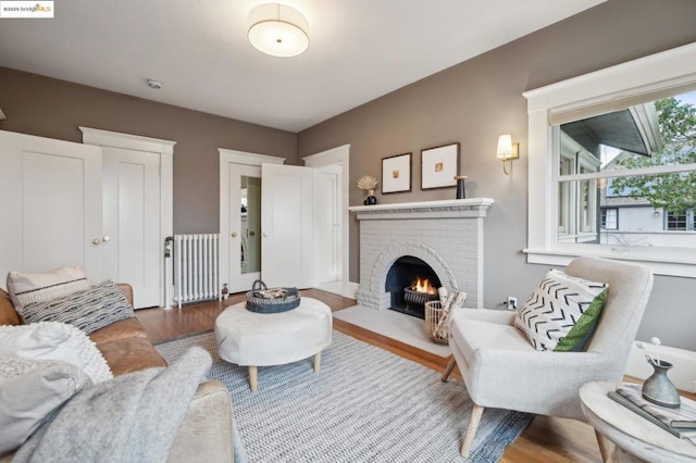 living room featuring hardwood / wood-style flooring, a brick fireplace, and radiator heating unit