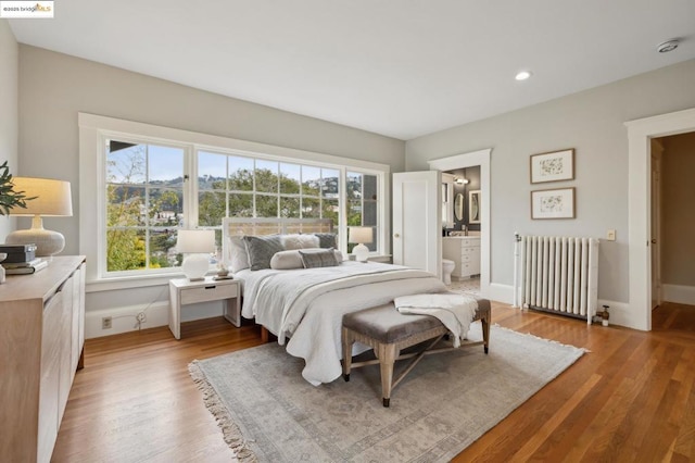 bedroom with light hardwood / wood-style flooring, ensuite bath, and radiator heating unit