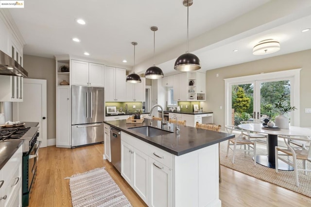 kitchen with decorative light fixtures, an island with sink, white cabinetry, sink, and stainless steel appliances