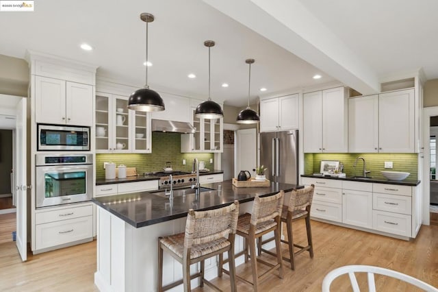 kitchen with an island with sink, sink, a kitchen breakfast bar, hanging light fixtures, and stainless steel appliances