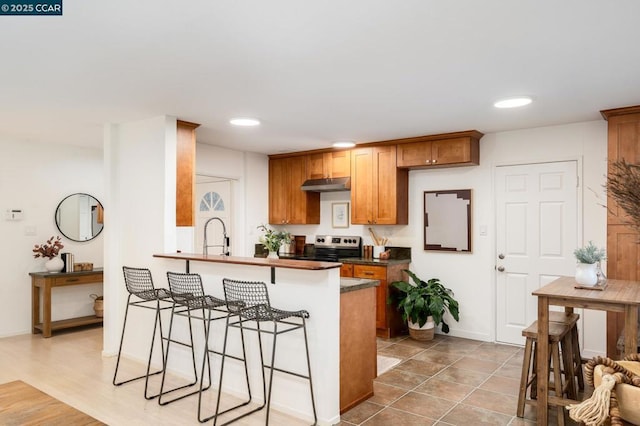 kitchen with light tile patterned floors, stainless steel range with electric cooktop, a kitchen bar, and kitchen peninsula