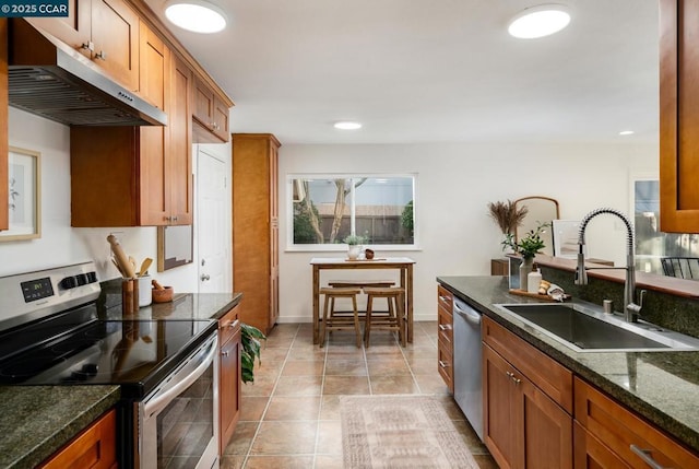 kitchen featuring dark stone countertops, sink, light tile patterned floors, and stainless steel appliances