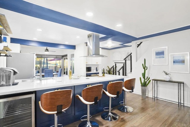 kitchen with white cabinets, island exhaust hood, beverage cooler, and a kitchen bar