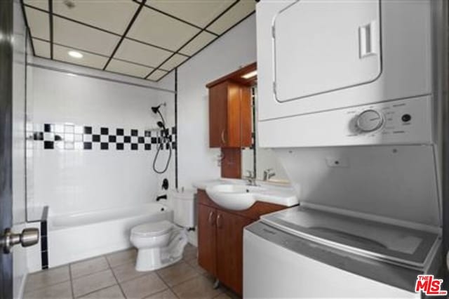 full bathroom featuring tiled shower / bath, vanity, stacked washer and clothes dryer, toilet, and tile patterned floors