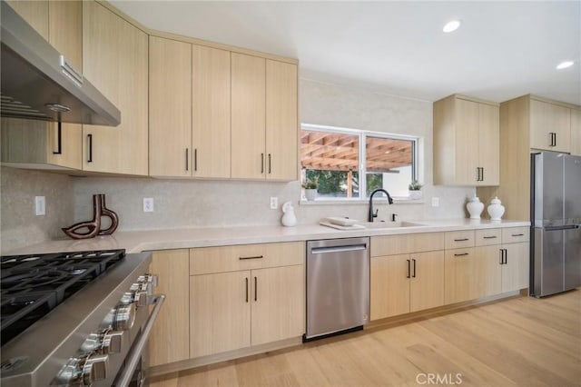 kitchen featuring appliances with stainless steel finishes, light brown cabinetry, tasteful backsplash, sink, and light hardwood / wood-style flooring