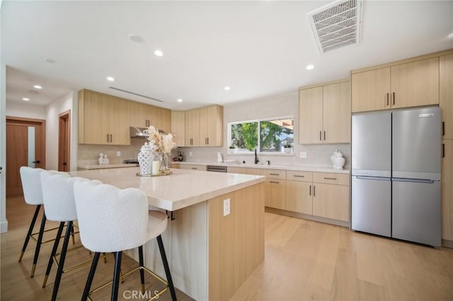 kitchen with a kitchen island, light brown cabinets, stainless steel fridge, and a kitchen breakfast bar