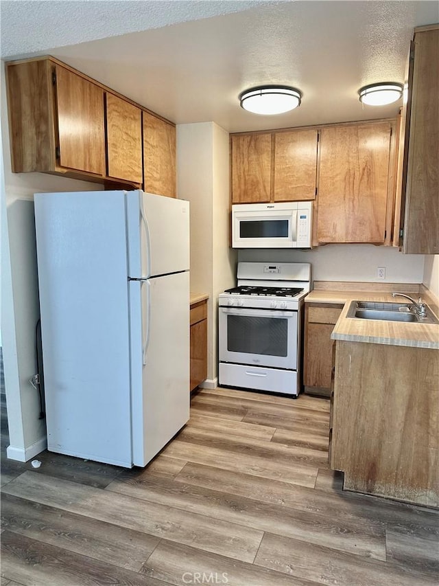 kitchen featuring sink, white appliances, light hardwood / wood-style floors, and a textured ceiling