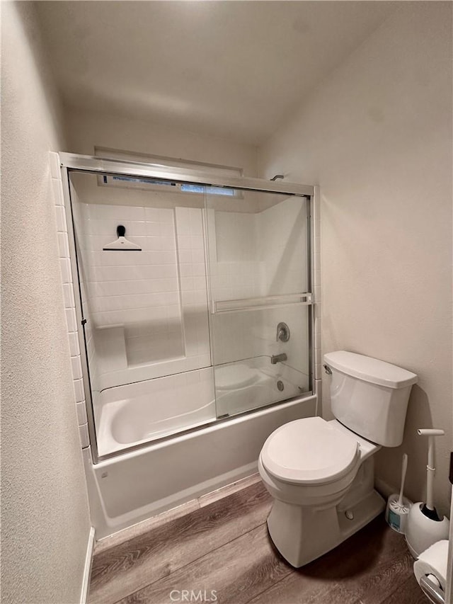 bathroom with hardwood / wood-style flooring, enclosed tub / shower combo, and toilet