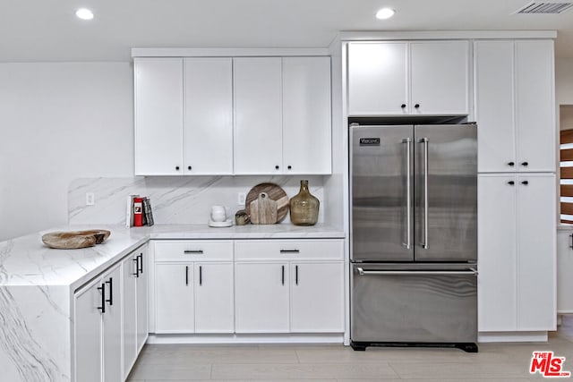 kitchen featuring white cabinetry, high end fridge, backsplash, and light stone counters