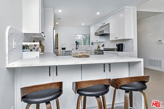 kitchen with a breakfast bar, high quality appliances, kitchen peninsula, range hood, and white cabinets