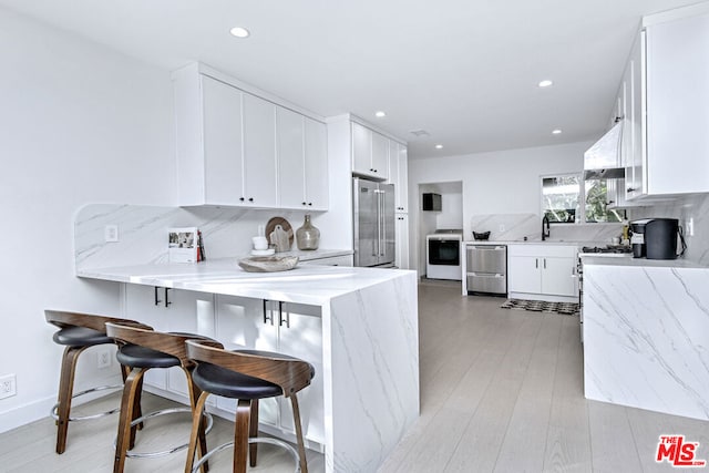 kitchen featuring a kitchen bar, white cabinetry, appliances with stainless steel finishes, kitchen peninsula, and decorative backsplash