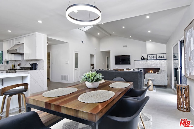 dining room with a tile fireplace, high vaulted ceiling, and light hardwood / wood-style floors