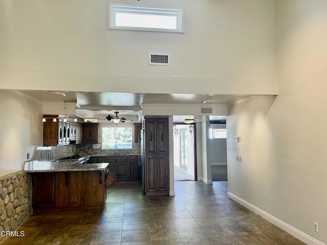 kitchen with stove, tasteful backsplash, light stone counters, ornamental molding, and kitchen peninsula