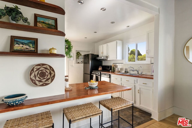 kitchen with white cabinetry, sink, a breakfast bar area, wooden counters, and stainless steel gas range