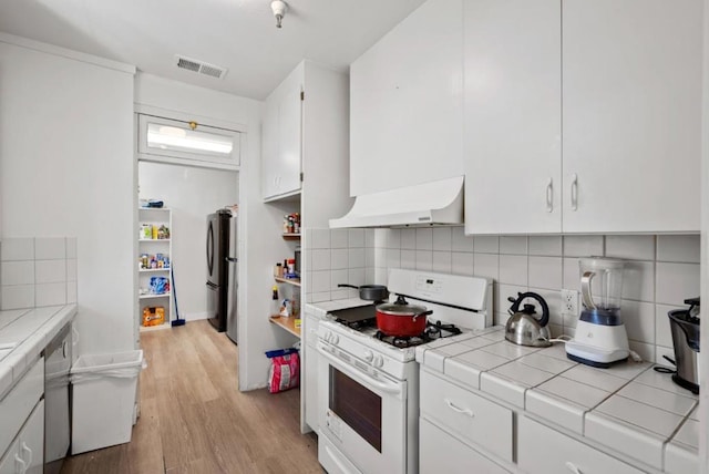 kitchen featuring stainless steel fridge, white range with gas stovetop, tile counters, white cabinets, and light wood-type flooring