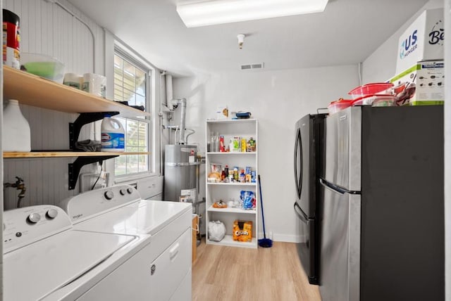 clothes washing area featuring strapped water heater, light hardwood / wood-style floors, and independent washer and dryer