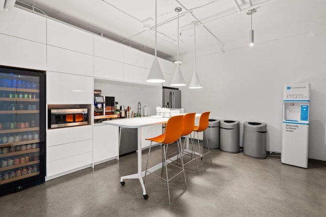 interior space with hanging light fixtures, a kitchen bar, white cabinets, and beverage cooler