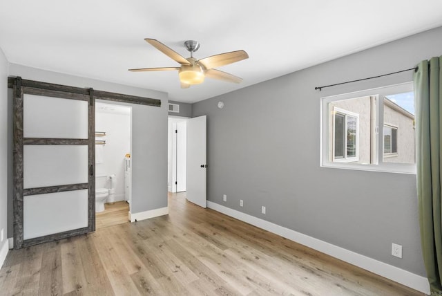 unfurnished bedroom featuring light hardwood / wood-style floors, a barn door, ceiling fan, and ensuite bathroom