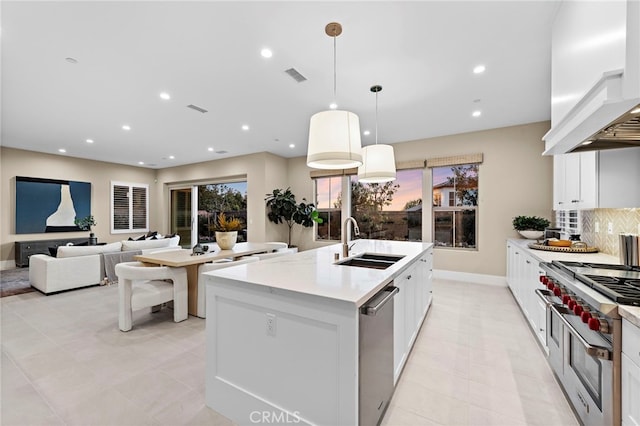 kitchen featuring appliances with stainless steel finishes, white cabinets, hanging light fixtures, custom range hood, and a center island with sink