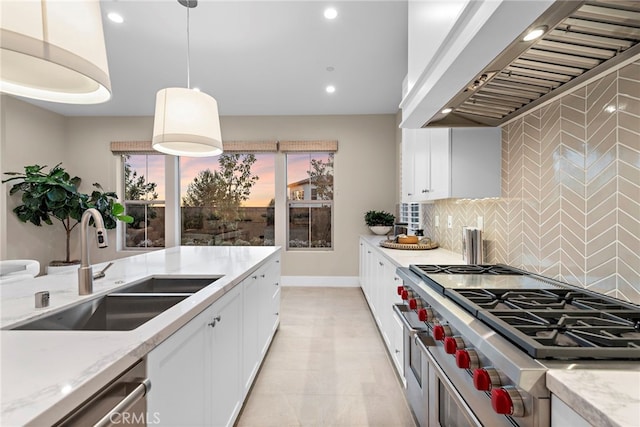 kitchen featuring wall chimney range hood, sink, appliances with stainless steel finishes, white cabinetry, and hanging light fixtures