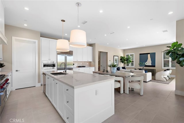 kitchen featuring sink, decorative light fixtures, appliances with stainless steel finishes, an island with sink, and white cabinets