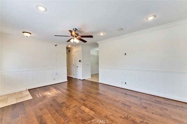 empty room with hardwood / wood-style flooring, ceiling fan, crown molding, and a wainscoted wall