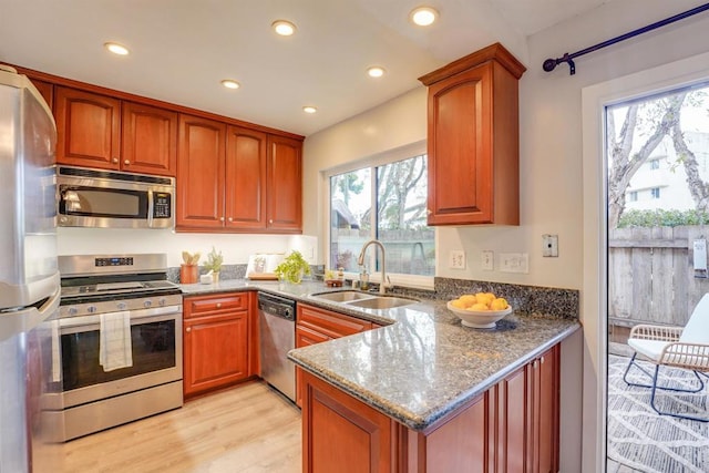 kitchen featuring stone counters, sink, kitchen peninsula, stainless steel appliances, and light hardwood / wood-style flooring