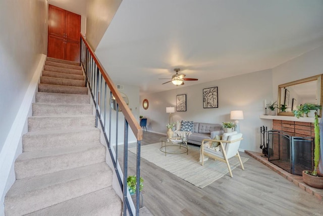 stairs featuring hardwood / wood-style flooring, a brick fireplace, and ceiling fan