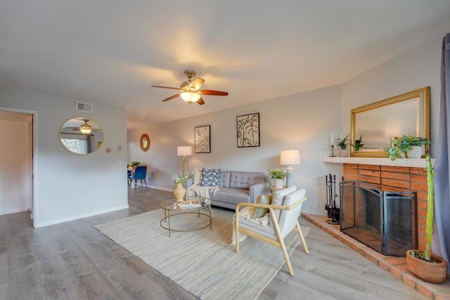 living room with hardwood / wood-style flooring, ceiling fan, and a brick fireplace