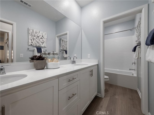 full bathroom with hardwood / wood-style flooring, vanity, shower / washtub combination, and toilet