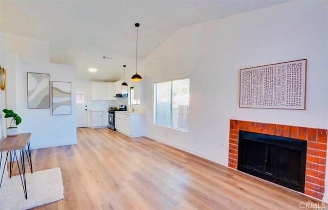 unfurnished living room with vaulted ceiling, a brick fireplace, and light hardwood / wood-style floors